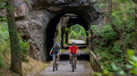 Dos personas en bicicleta pasan por uno de los t�neles sobre una antigua v�a de ferrocarril minero, situado en pleno trazado de la V�a Verde de la Senda del Oso