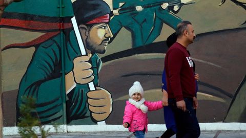 Una familia camina ante un mural en Teher�n, la capital de la rep�blica isl�mica