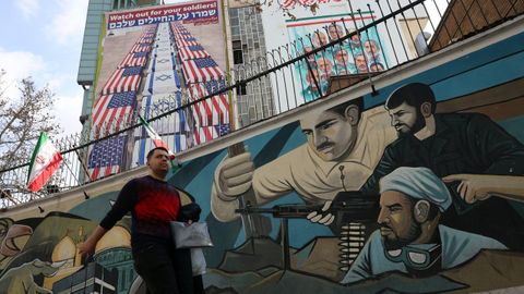 Un iran� pasa por un mural dedicado a los soldados cerca de carteles antiamericanos e israel�es.