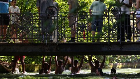 Varias personas se asoman a un puente sobre el arroyo Eisbach en el Jard�n Ingl�s de M�nich (Alemania).