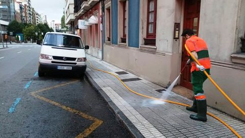 Un operario de Emulsa realiza un baldeo en una acera de Gijn