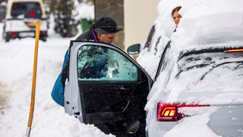 Un hombre despeja la nieve para poder acceder a su vehículo en el pueblo de Pajares (Asturias), que se encuentra en nivel rojo, lo cual implica la prohibición de circulación de vehículos articulados, camiones y autobuses.