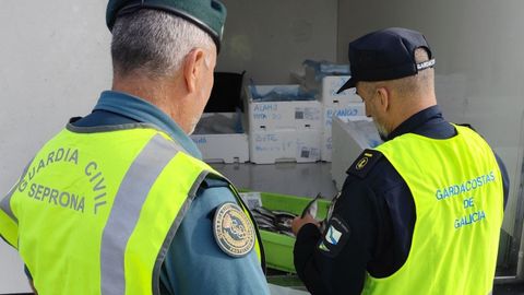 Un agente de la Guardia Civil y otro de Gardacostas de Galicia manipulan parte del pescado decomisado en Xove