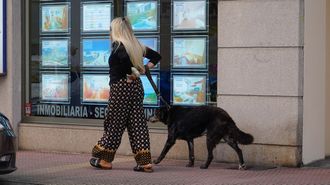 Una mujer con su perro, paseando por una calle en la que hay un negocio inmobiliairo