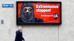 Unas personas pasan en Z�rich ante un cartel de los partidarios de suprimir el burka en Suiza