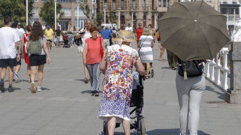 Una mujer se protege con un paraguas mientas pasea por el Muro de San Lorenzo en Gijón