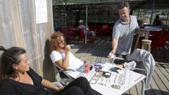 Pichu Gonz�lez, atendiendo a dos clientas en la terraza de su bar, O Alpedre, situado en la playa de Doni�os