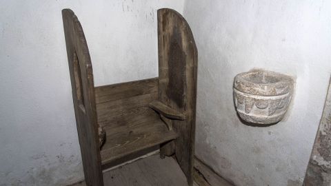 Un antiguo confesionario y una pila en el interior de la iglesia