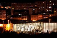 El edificio cultural �gora, en primer plano, iluminado, con el barrio del Agra al fondo. 