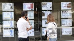 Dos personas mirando ofertas de pisos en el escaparate de una inmobiliaria de Lugo