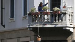 Una mujer tira por la cuerda con la que sostiene un cesto que utiliza para que los viandantes le depositen comida, en Mil�n