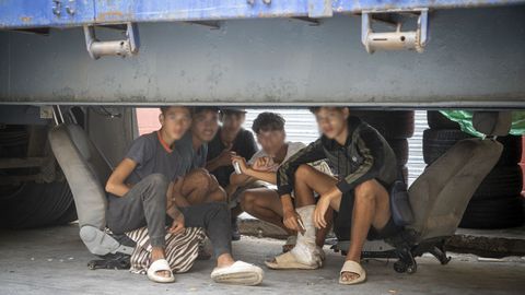 Cinco migrantes menores de edad se protegen de la lluvia debajo de un remolque en Ceuta.