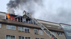 Bombero extinguiendo desde lo alto de la escalera el incendio, ante la mirada de vecinos de la terraza contigua.