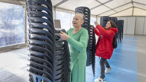 Chus Iglesias (en primer plano, de verde) y una ayudante colocando esta ma&ntilde;ana las sillas para celebrar esta noche la cena solidaria de Nochebuena en la carpa de la Alameda.