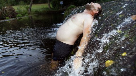 Un hombre se refresca bajo la cascada de la presa del r�o Asma, en Chantada