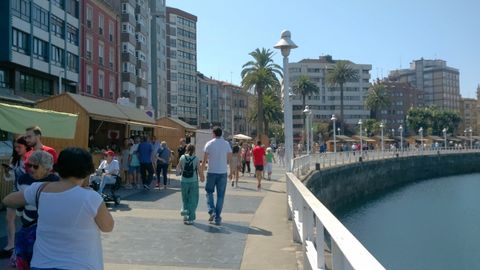 Paseantes  por el puerto deportivo, con el Mercadín de la Sidra y la Manzana del Festival de la Sidra