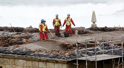 Los operarios depositan tejas sobre los muros laterales para evitar que les entre el agua.