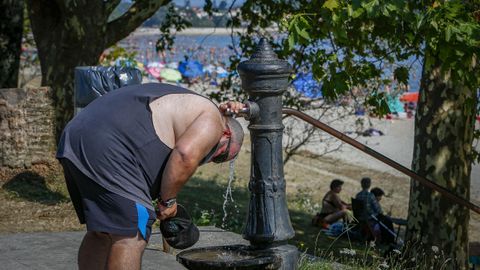 Un hombre se refresca en una fuente en la playa de Barraña, en Boiro