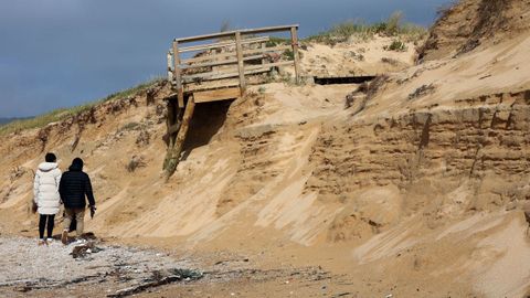 Dos vecinos de la zona paseaban el jueves por la playa de A Lanzada, en O Grove, al lado de una duna sobre la que se encuentra el paseo de madera arrasado. La arena est� cubierta de residuos.