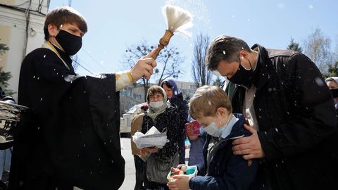 Un clrigo con una mascarilla echa agua bendita sobre los creyentes durante una ceremonia para bendecir los pasteles y los huevos de Pascua en la vspera de la Pascua ortodoxa, en Stavropol, Rusia