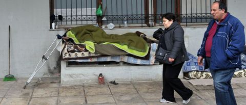 Dos personas con la vista en el suelo caminan por una calle donde descansa un sintecho en la ciudad de Salnica. 