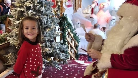 Pap Noel lee con detalle la lista de regalos que le piden los pequeos visitantes