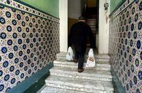 Un anciano cargado con bolsas de la compra enfila las escaleras de su portal