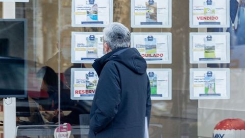 Un hombre observa los carteles de alquiler y venta de vivienda de una oficina inmobiliaria.