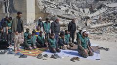 Un grupo de voluntarios de la milicia isl�mica reza al lado de un edificio destruido por los bombarderos