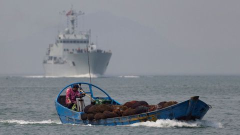 Un barco de pesca pasa junto a un buque de guerra chino durante unas maniobras militares en el estrecho de Taiwn.