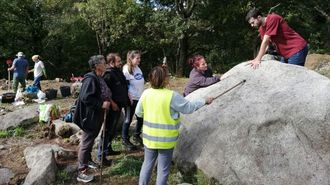 El fil&oacute;logo &Aacute;lvaro Lorenzo (a la derecha) muestra la inscripci&oacute;n de la roca de O Preguntoiro a un grupo de vecinos de Pombeiro durante una reciente visita guiada al yacimiento medieval
