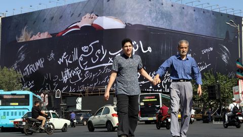 Dos iran&iacute;es dejan atr&aacute;s una pancarta propagand&iacute;stica de a Trump en un ata&uacute;d. 