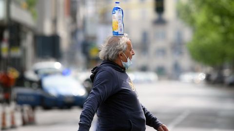 Un hombre con la mascarilla en el mentn y una botella en la cabeza cruza una calle en Miln, Italia