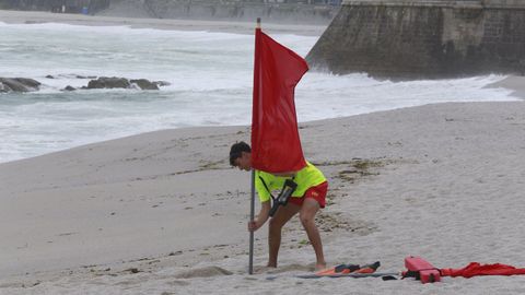 Un socorrista clava la bandera roja en la playa de Riazor-Orzán en el primer día de servicio de este verano.