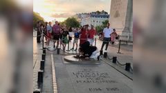 El hombre, de rodillas, encendindose el cigarrillo con la llama del monumento.