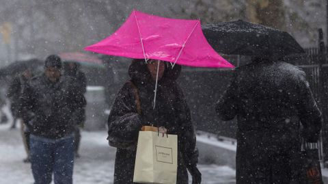 Una mujer camina con su paraguas roto bajo la nieve.