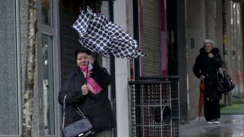 Una mujer y su paraguas pelean contra el viento esta maana en A Corua