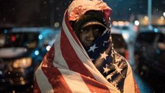 Un manifestante cubierto con la bandera de Estado Unidos protesta frente a un departamento de la polic�a en Misuri.