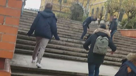 Un polica agrede con un tolete a una persona tirada en el suelo, ante la mirada de una segunda persona y varios universitarios que se les acercan