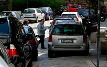 Varios transe�ntes pasan entre los coches aparcados en la plaza de Azc�rraga. 