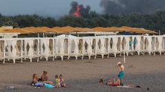La gente descansa en una playa mientras el humo y las llamas se elevan despus de las explosiones en una base area militar rusa, en Novofedorivka, en Crimea.  
