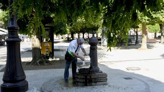 Un hombre, llenado una botella con agua de una fuente en Lugo.