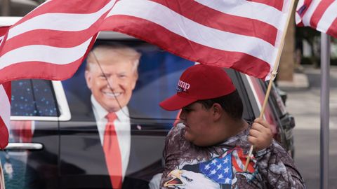 Un seguidor de Trump ondea una bandera de EE.UU. junto a un veh�culo rotulado con la imagen del expresidente republicano