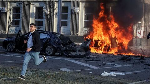 Imagen de archivo de un hombre corriendo por una calle del centro de Kiev mientras a su espalda arde un coche alcanzado por un proyectil ruso.