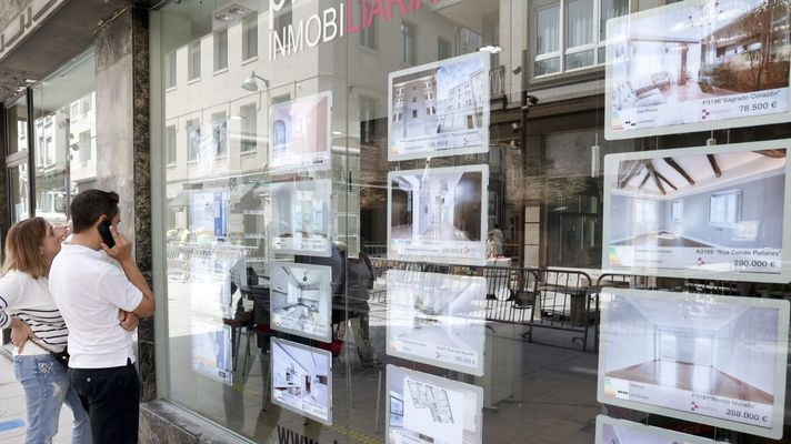 Personas mirando ofertas de pisos en el escaparate de una inmobiliaria.