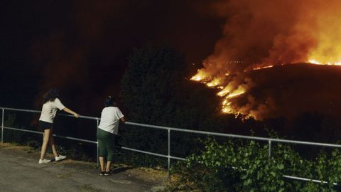 Dos personas observan el fuego que afecta al pueblo de Chas, Vilaza