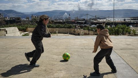 Dos ni�os juegan este lunes al f�tbol en un recinto para personas desplazadas por la guerra, de fondo, una columna de humo por un bombardeo israel�.