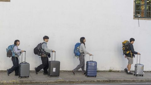 Un grupo de turistas pasea con sus maletas por una calle del centro histrico compostelano.