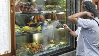 Clientes mirando mariscos, pescados y carnes en el escaparate de un restaurante compostelano.