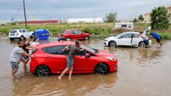 Varias personas empujan sus coches afectados por la tromba de agua en Pueblo de Sagunto